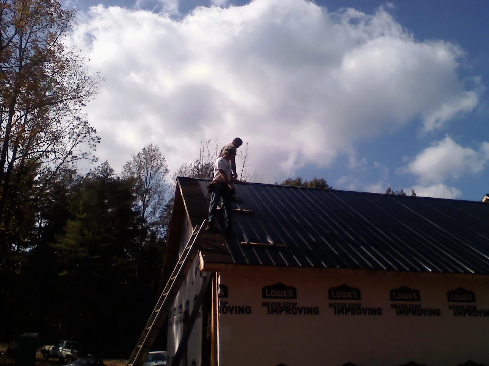 Roofer fastening dark metal panels high against a cloudy sky, from a Roof Inspection job in Oakland